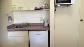 Une petite cuisine équipée comprenant un évier, un petit réfrigérateur, un four à micro-ondes et une bouilloire.