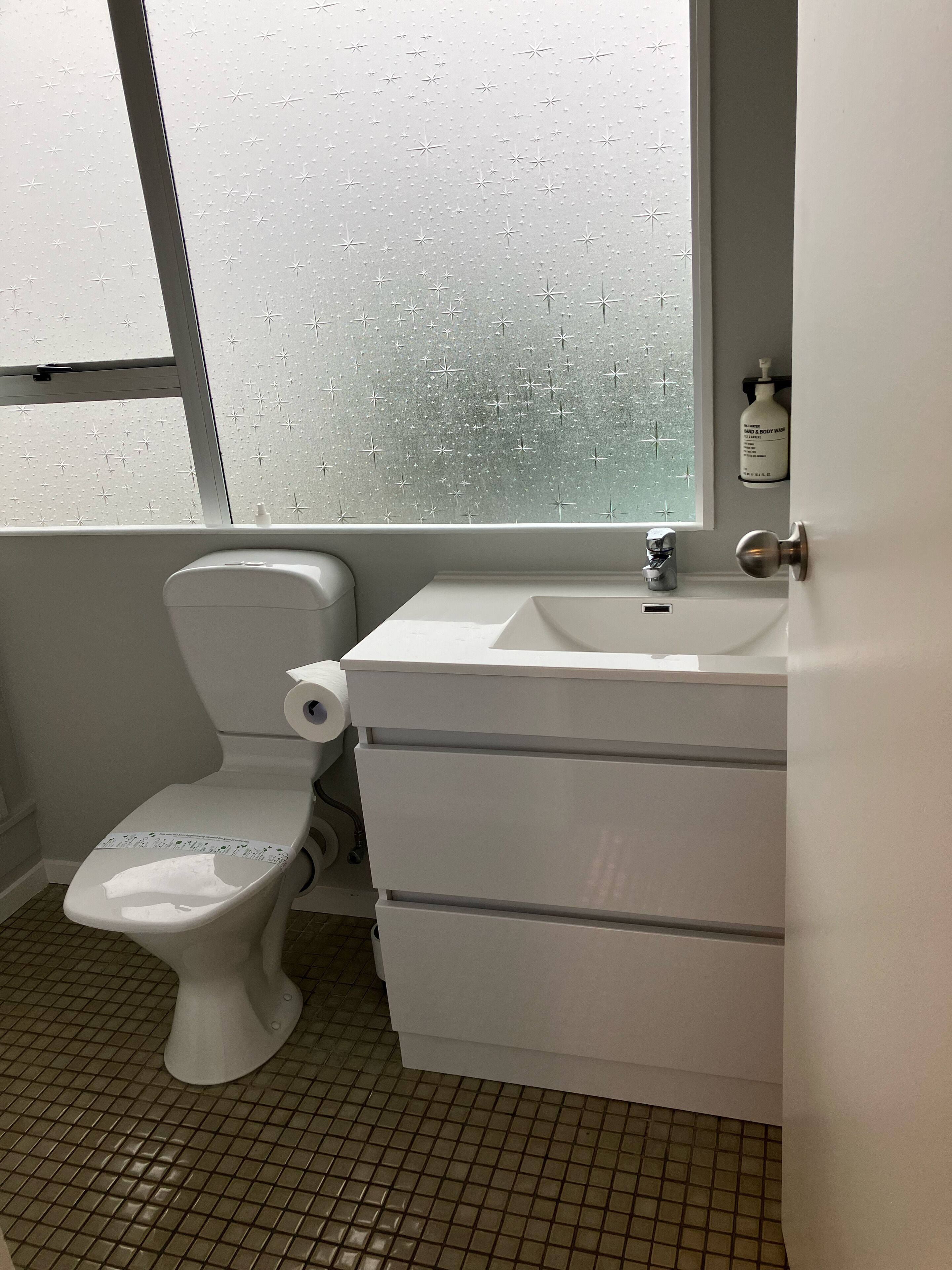 Un baño con inodoro, lavabo y ventana con vidrio esmerilado.