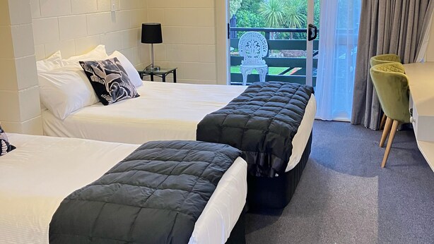 Habitación de hotel con dos camas, una mesita con lámpara, una silla y vistas al exterior.
