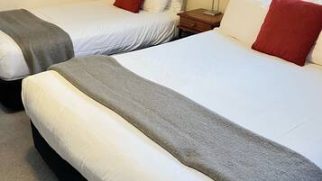 Two single beds with white linens and red pillows, a nightstand with a lamp, and a red curtain on the wall.
