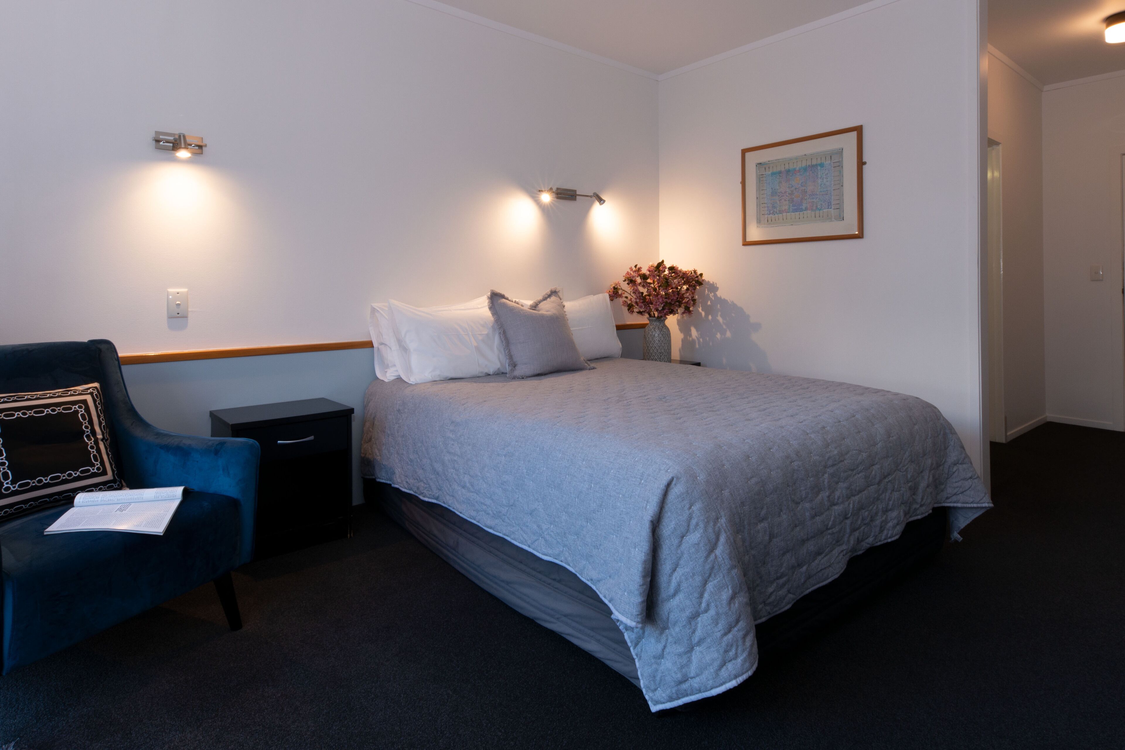 A bedroom with a bed, bedside tables, a chair, a vase with flowers, and a framed picture on the wall.