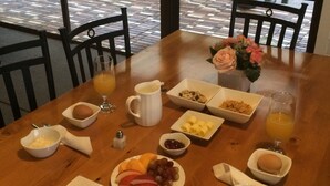A breakfast table with a variety of food items, including bread, fruit, and a glass of orange juice. - Aotearoa Lodge (Whitianga)