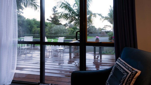 A room with a view of a wooden deck and outdoor seating area. - Aotearoa Lodge (Whitianga)
