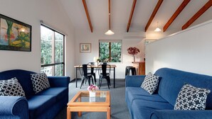 A living room with two blue sofas, a wooden coffee table, and a dining area with a table and chairs. - Aotearoa Lodge (Whitianga)