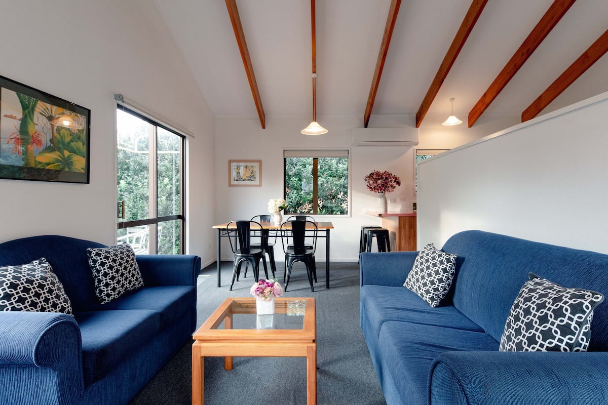 A living room with two blue sofas, a wooden coffee table, and a dining area with a table and chairs.