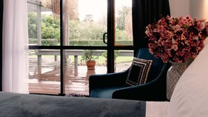 A room with a large window, a blue armchair, a potted plant, and a white bed. - Aotearoa Lodge (Whitianga)