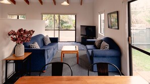 A modern living room with a blue sofa set, a wooden coffee table, and a TV on a stand. - Aotearoa Lodge (Whitianga)