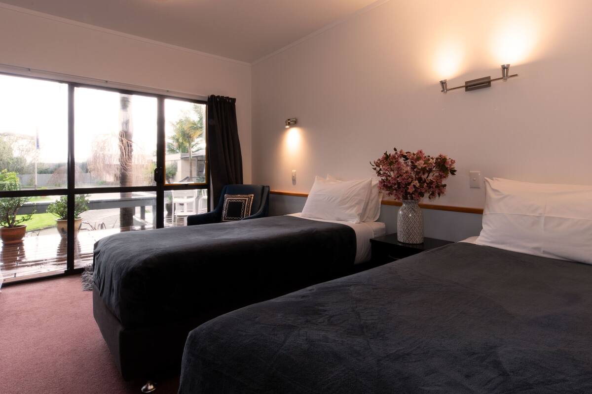 A hotel room with two beds, a large window, a vase with flowers, and a nightstand.