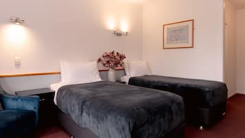 A hotel room with two beds, a nightstand, a chair, and a vase with flowers.