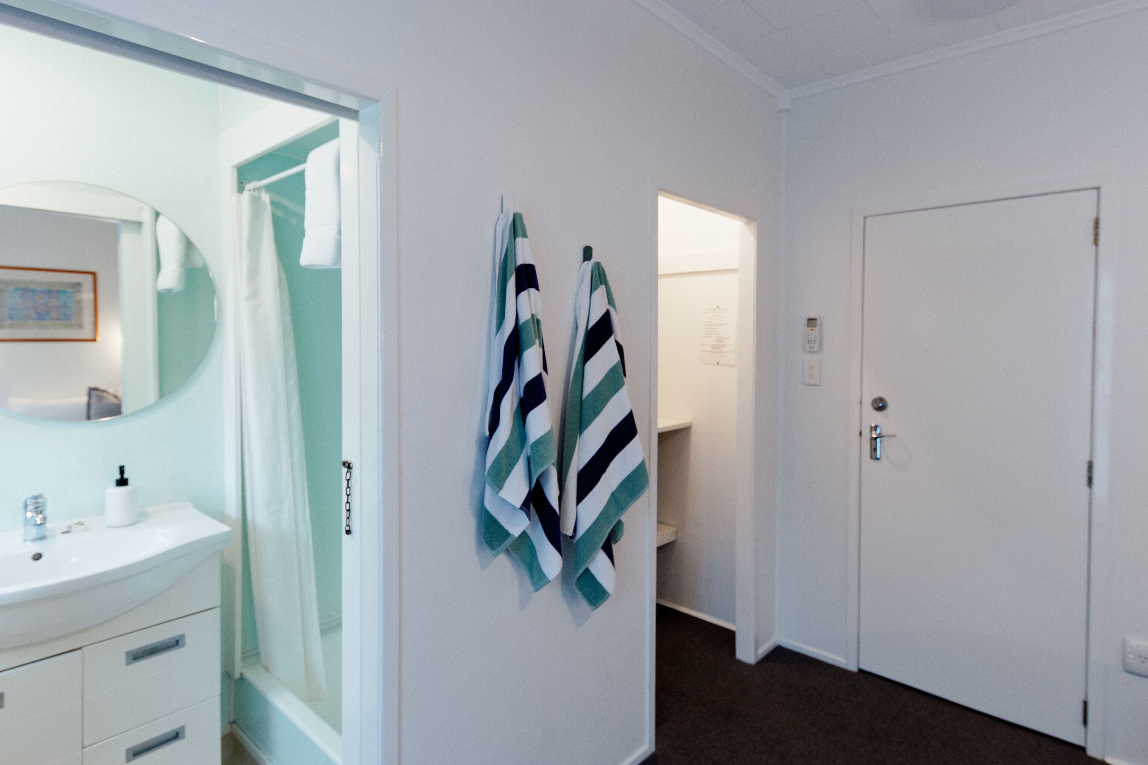 A hotel room with a bathroom, a shower, a sink with a mirror, and a door.