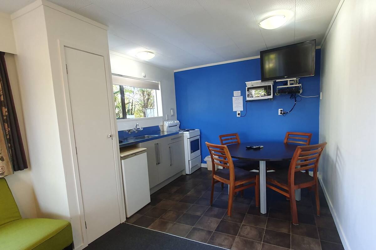 A compact kitchen with a dining area, a microwave, a TV, and a window with a view of greenery.
