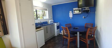 A compact kitchen with a dining area, a microwave, a TV, and a window with a view of greenery.