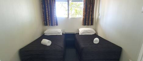 Ein kleines, sauberes Zimmer mit zwei Einzelbetten, einem Fenster mit Vorhängen und Teppichboden.