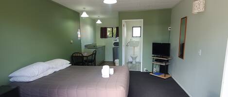 Una camera da letto con un letto, una scrivania, una sedia, una TV e un bagno parzialmente visibile da una porta aperta.
