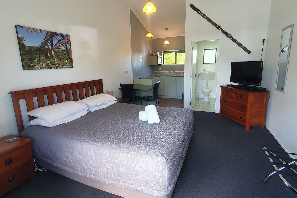 A bedroom with a bed, a nightstand, a dresser, a TV, and a painting on the wall.