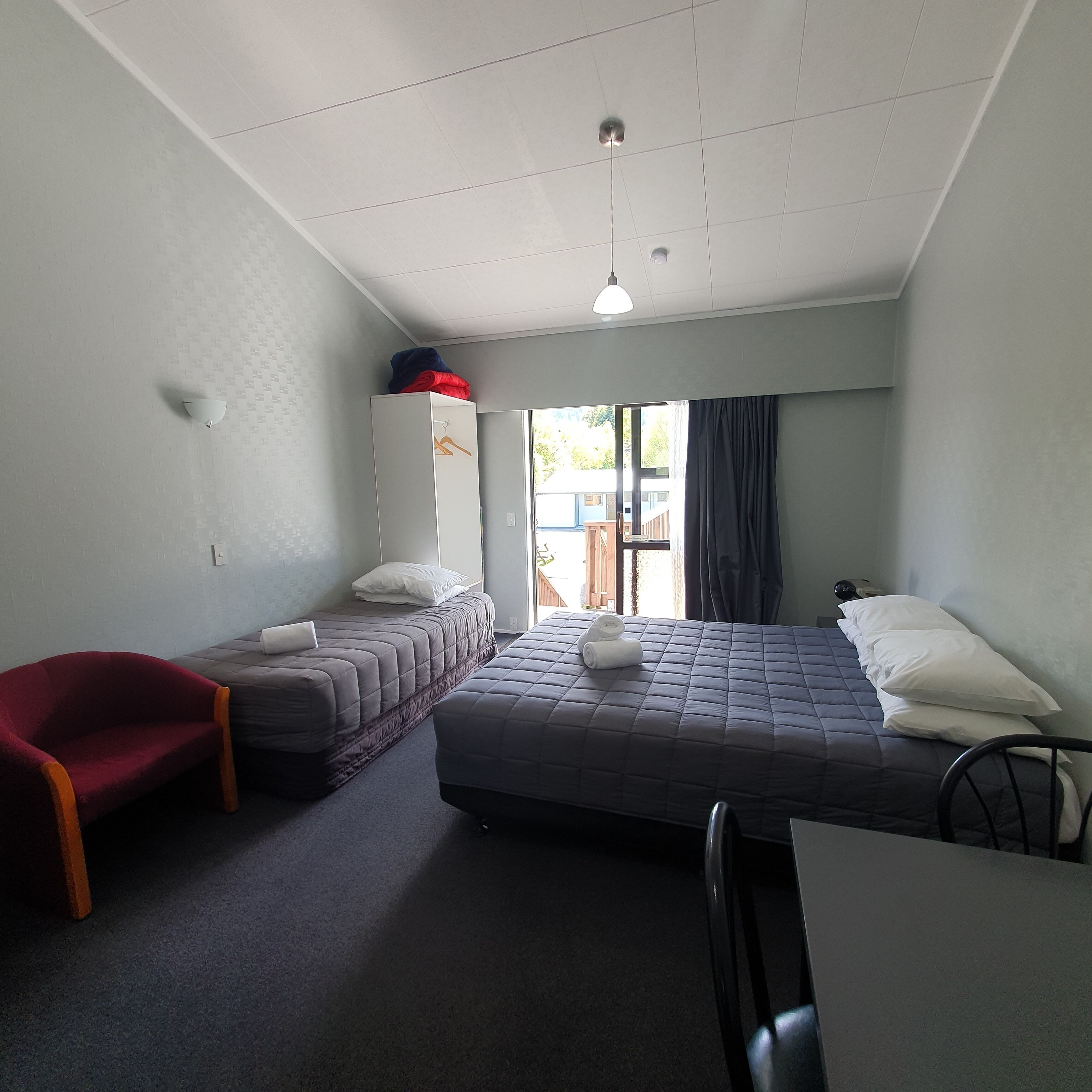 A small, well-lit room with two beds, a desk, a chair, and a wardrobe.