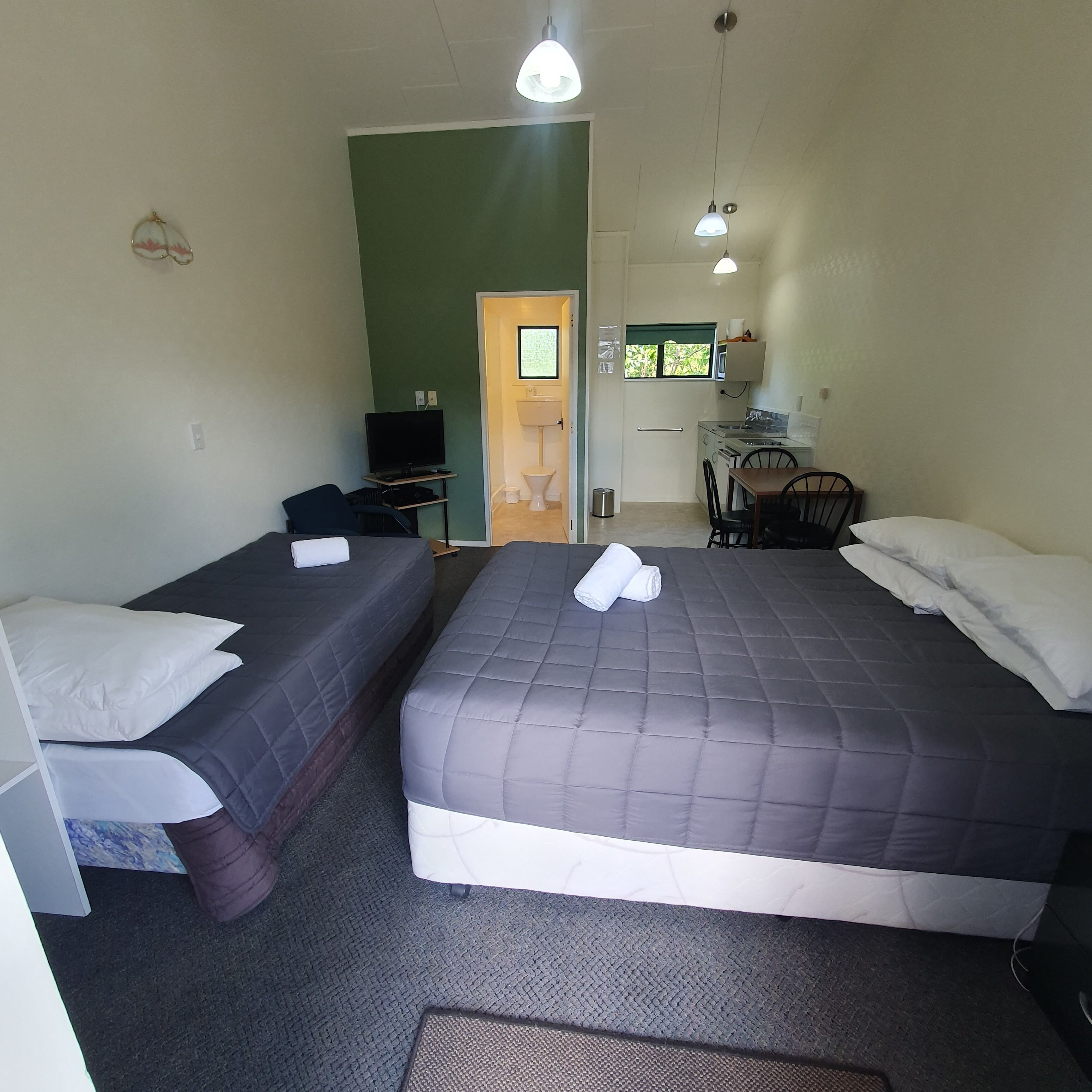 A room with two beds, a desk with a computer, a small kitchenette, and a door leading to a bathroom.