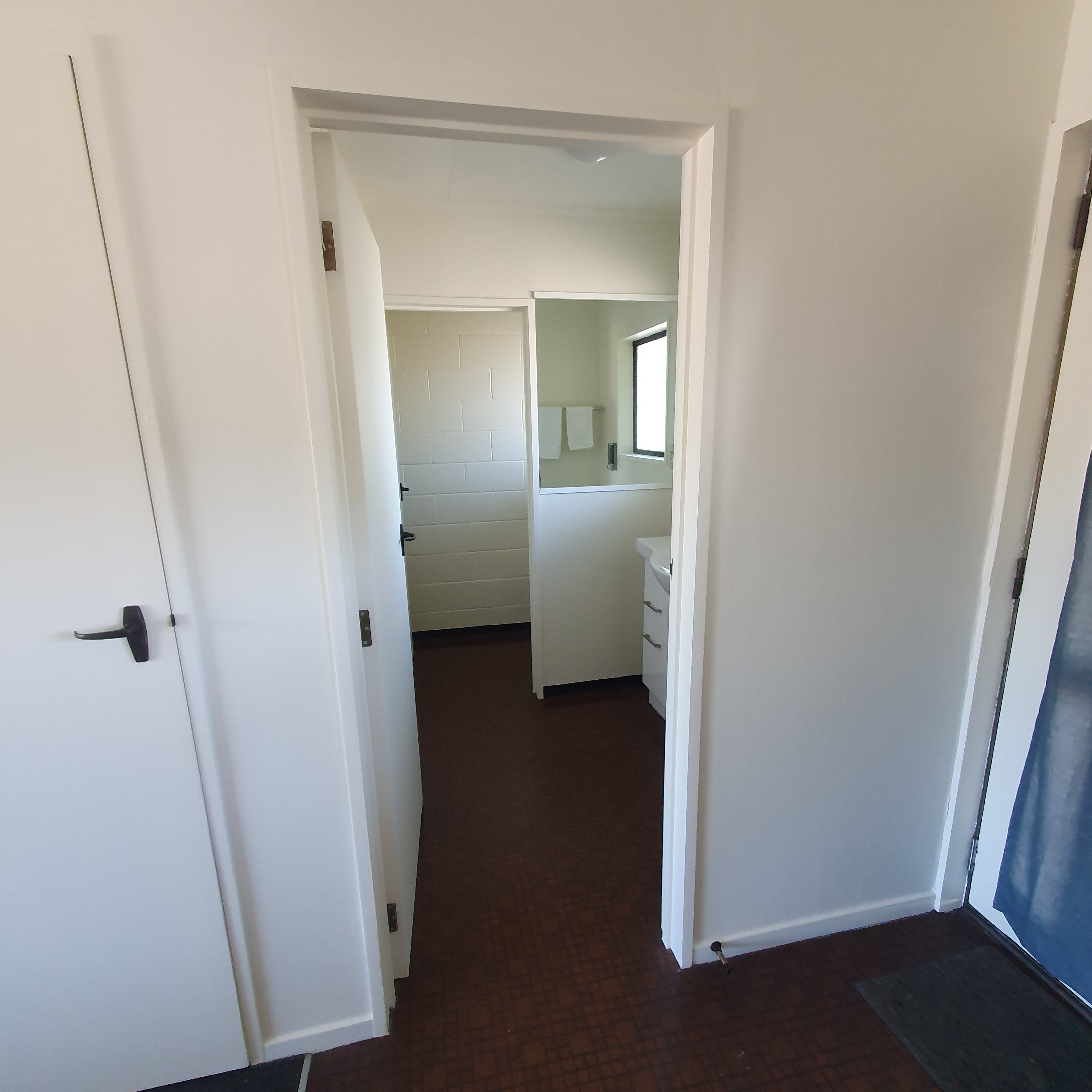 Un pasillo que conduce a un baño con una puerta blanca, un ventanal y suelo de baldosas.
