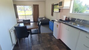 Una cocina compacta con mesa, sillas, microondas, pileta y ventana con vista a la vegetación.
