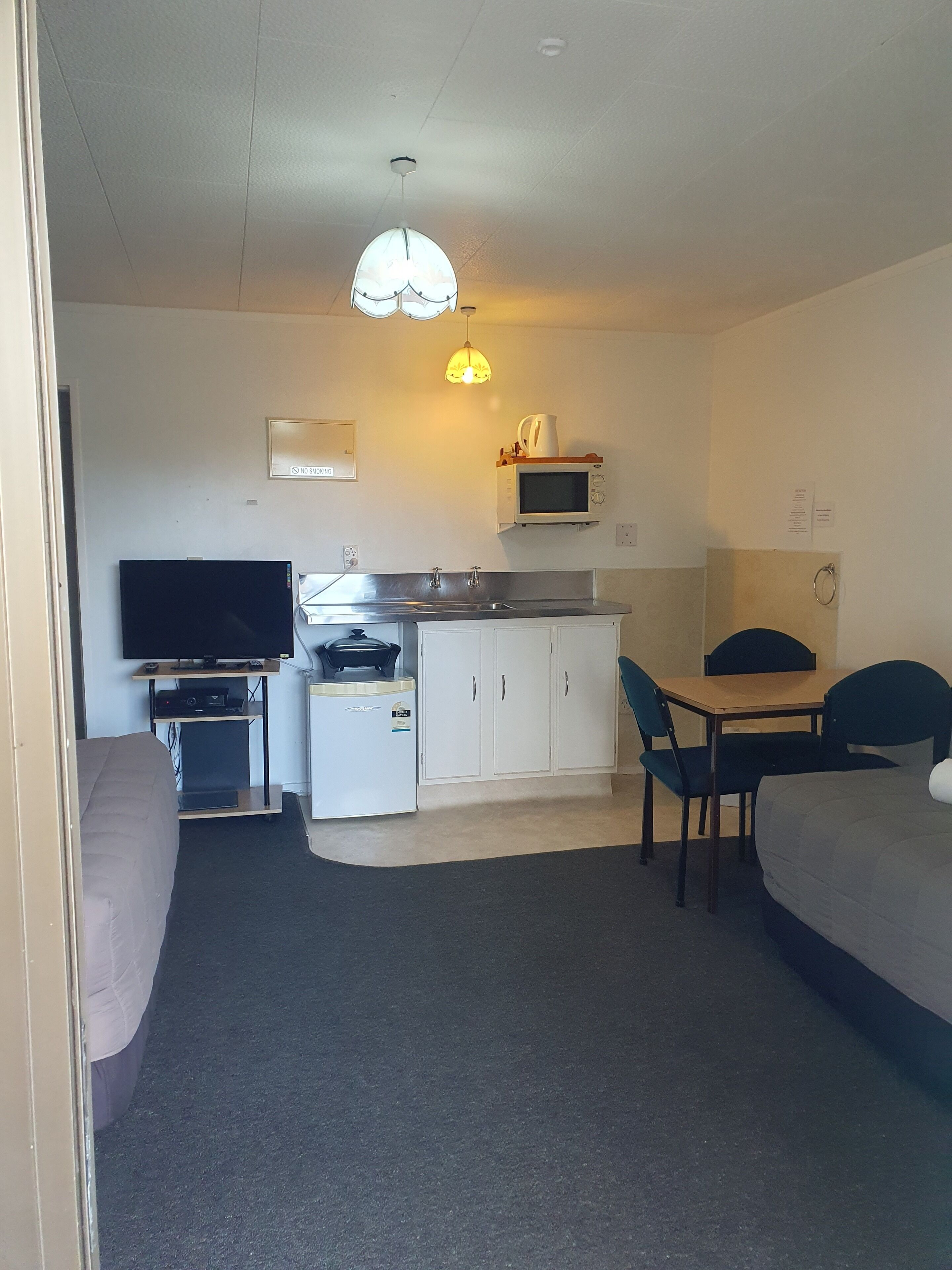 A compact room with a kitchenette, a dining area, a television, and a bed.