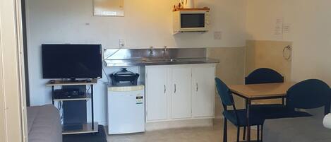 A compact room with a kitchenette, a dining area, a television, and a bed.