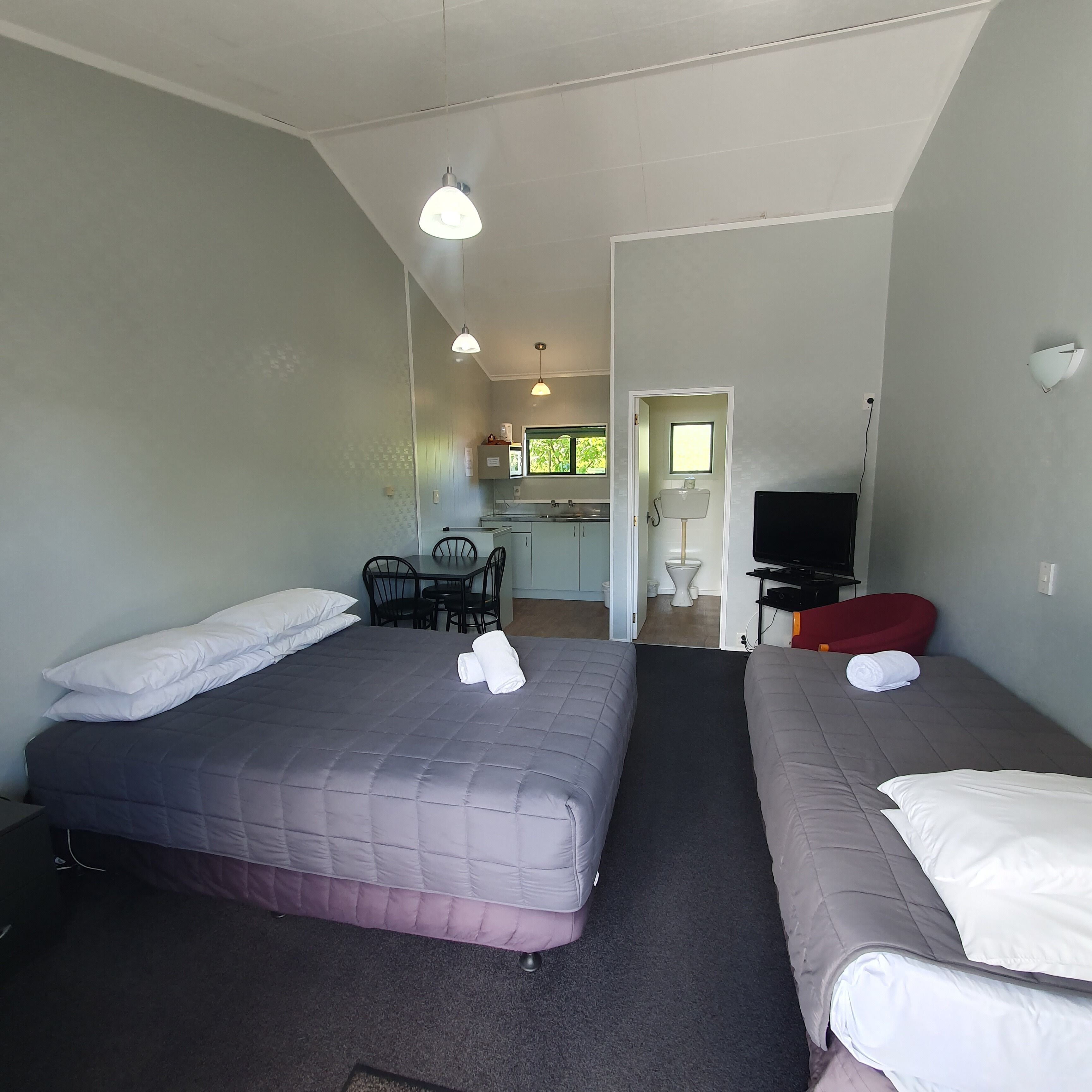 A hotel room with two beds, a desk, a chair, a television, and a small kitchenette.
