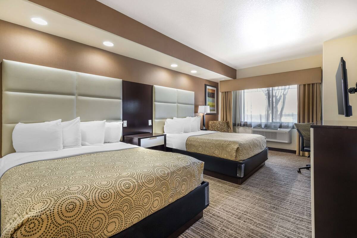 Une chambre d’hôtel avec deux lits, une grande fenêtre avec des rideaux, un téléviseur à écran plat et un bureau avec une lampe.