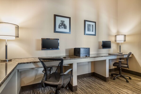 A hotel room with a desk, two chairs, a printer, and two framed pictures on the wall.