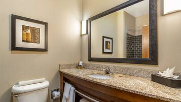 A bathroom with a toilet, sink, mirror, framed artwork, and towels.