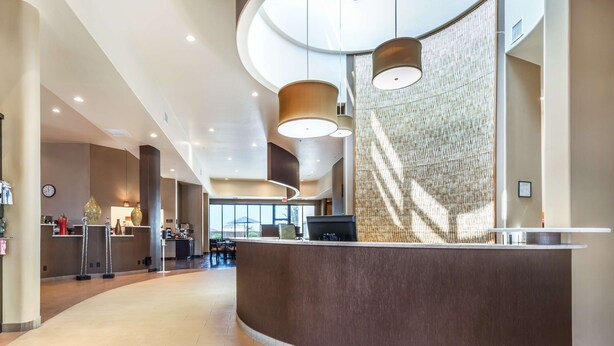 Eine moderne Hotelhalle mit einer gebogenen Rezeption, großen Pendelleuchten und einer Wanddekoration.