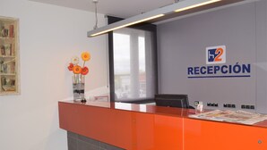 Un mostrador de recepción con una vitrina de vidrio que contiene flores, una ventana y un letrero en la pared que dice "RECEPCIÓN".