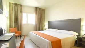 Habitación de hotel con cama, escritorio, laptop, silla y ventana con cortinas.