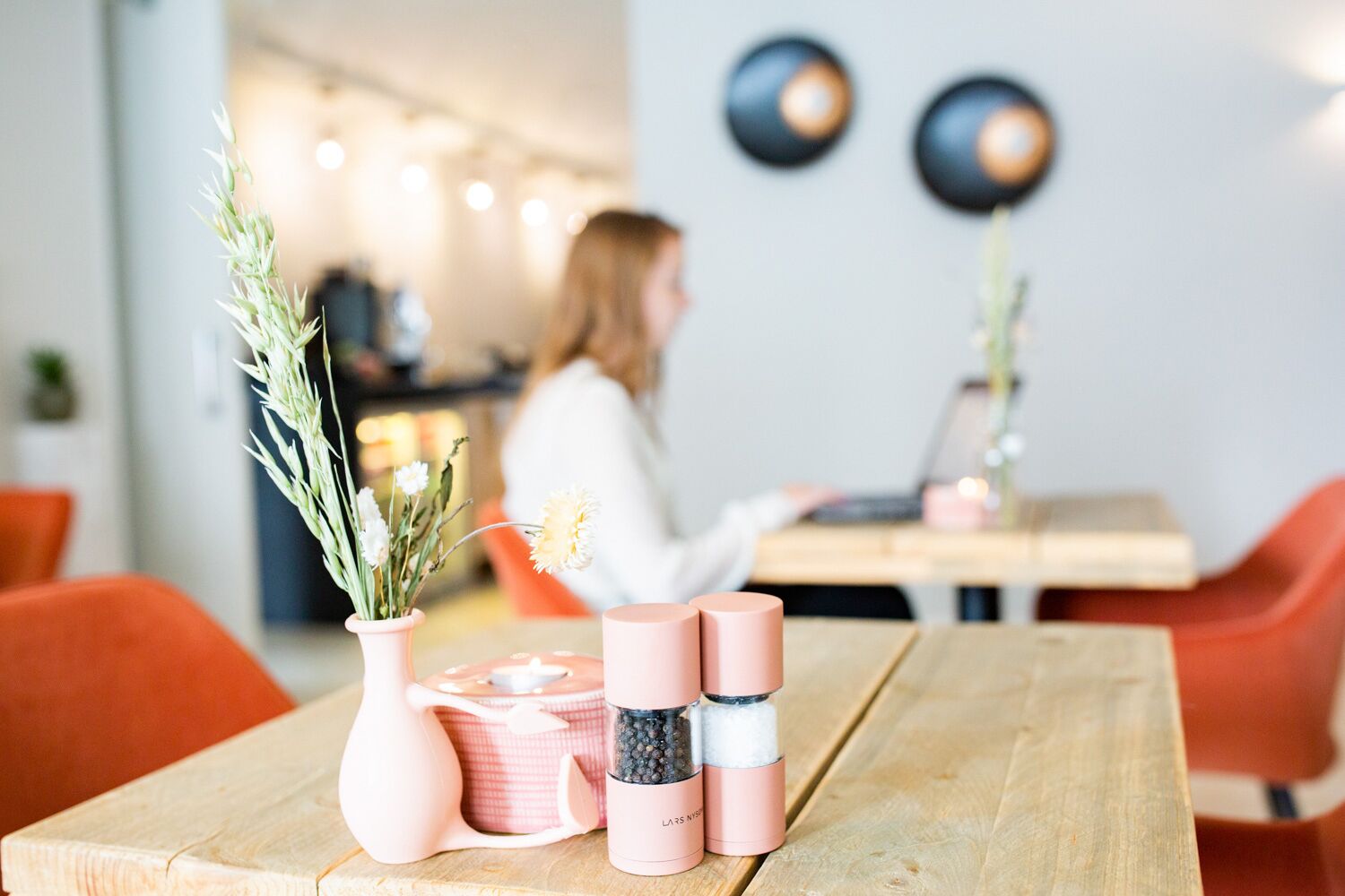 A wooden table with a pink vase, a pink container, and a pink candle holder.