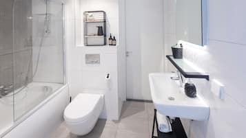 Ein modernes Badezimmer mit einer gläsernen Duschkabine, einer weißen Toilette, einem Waschbecken mit schwarzer Arbeitsplatte und einem Spiegel darüber.