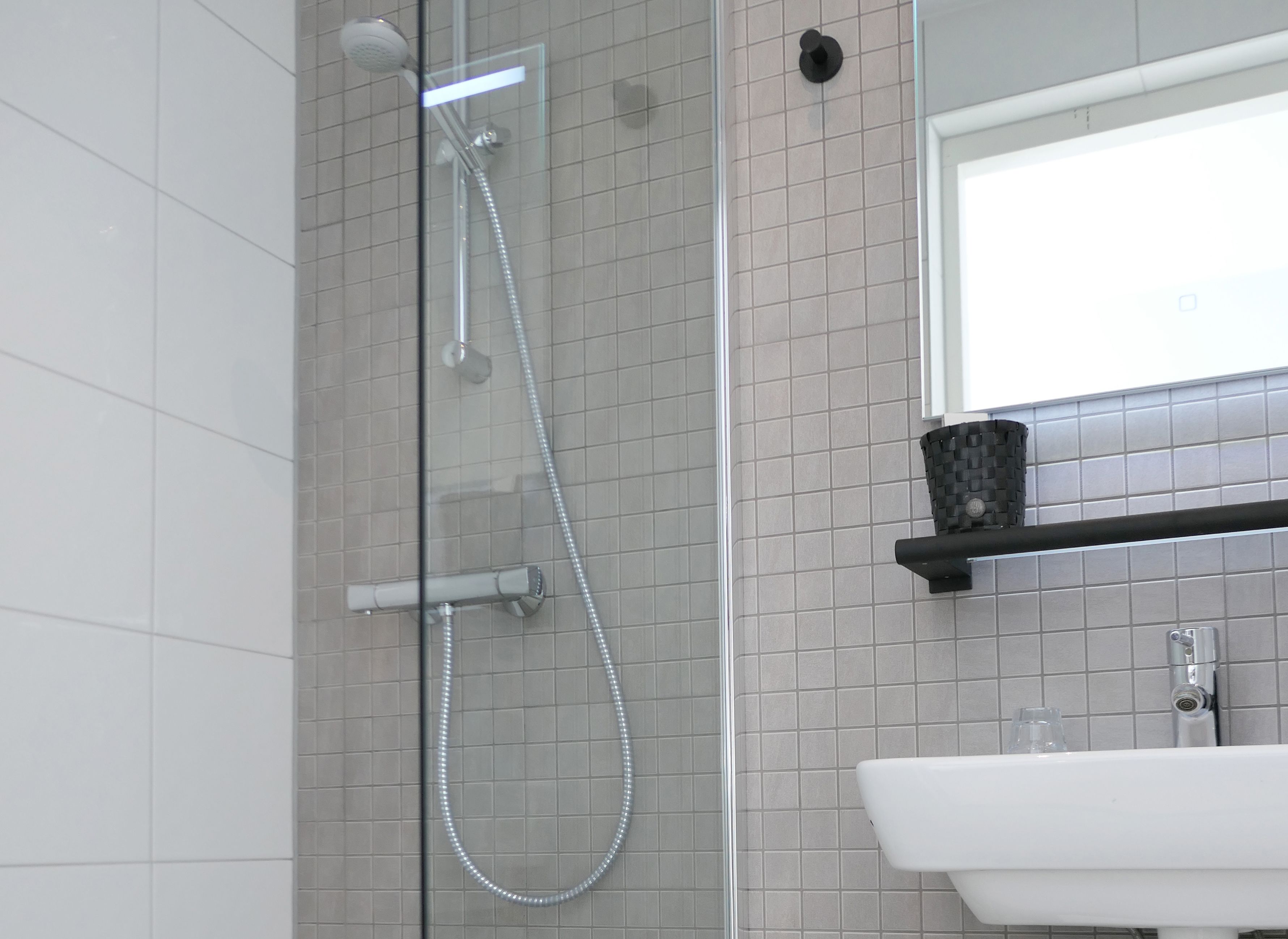Une salle de bain moderne avec une douche à parois de verre, un lavabo blanc et un mur recouvert de carreaux.