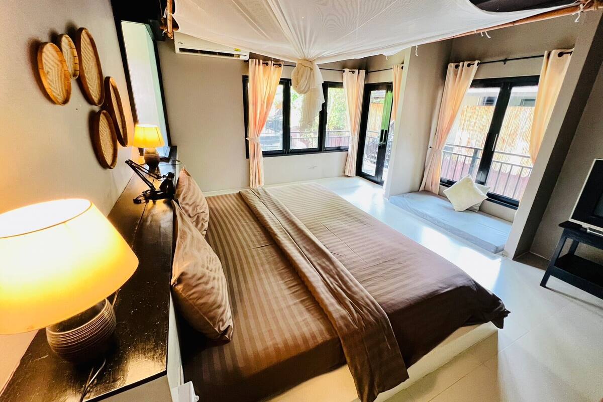 A bedroom with a bed, bedside lamp, curtains, and a view of the outside.