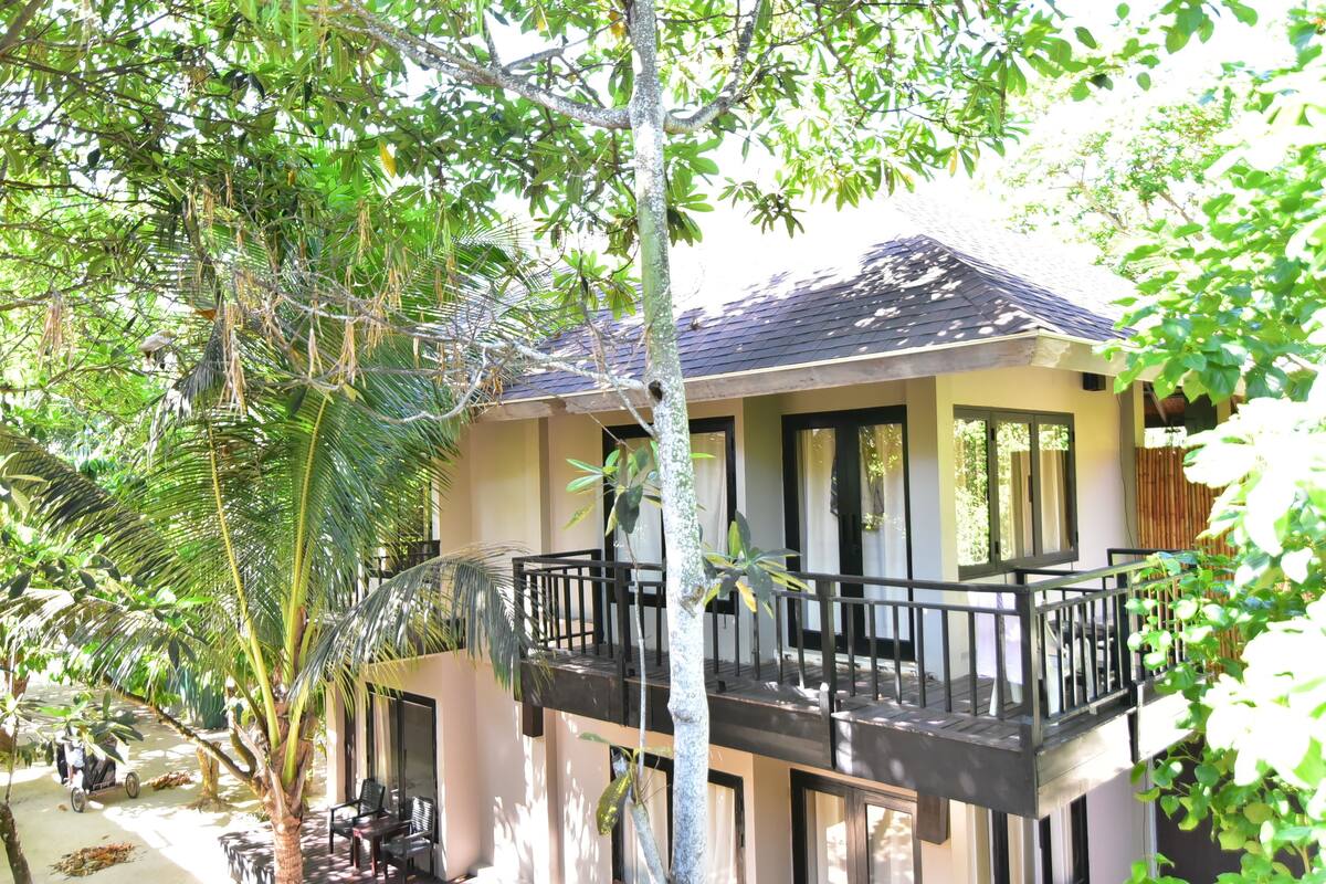 A two-story building with a balcony, surrounded by lush greenery.