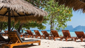 Una playa con sillones de madera y una sombrilla de paja.