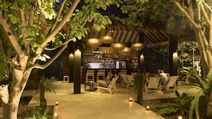 Zona de bar al aire libre con asientos y techo de paja.