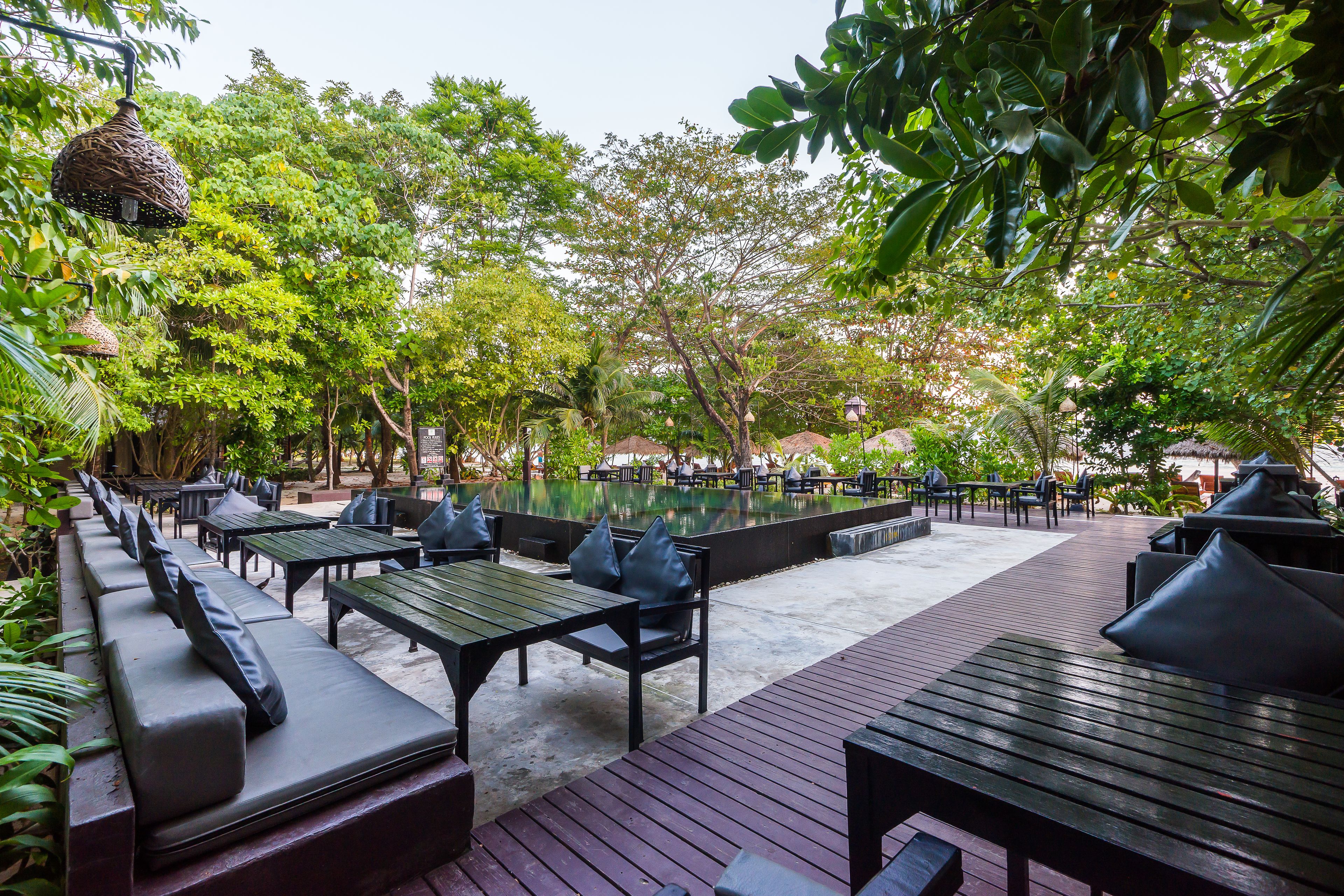 An outdoor seating area with wooden tables and benches, surrounded by lush greenery and trees.