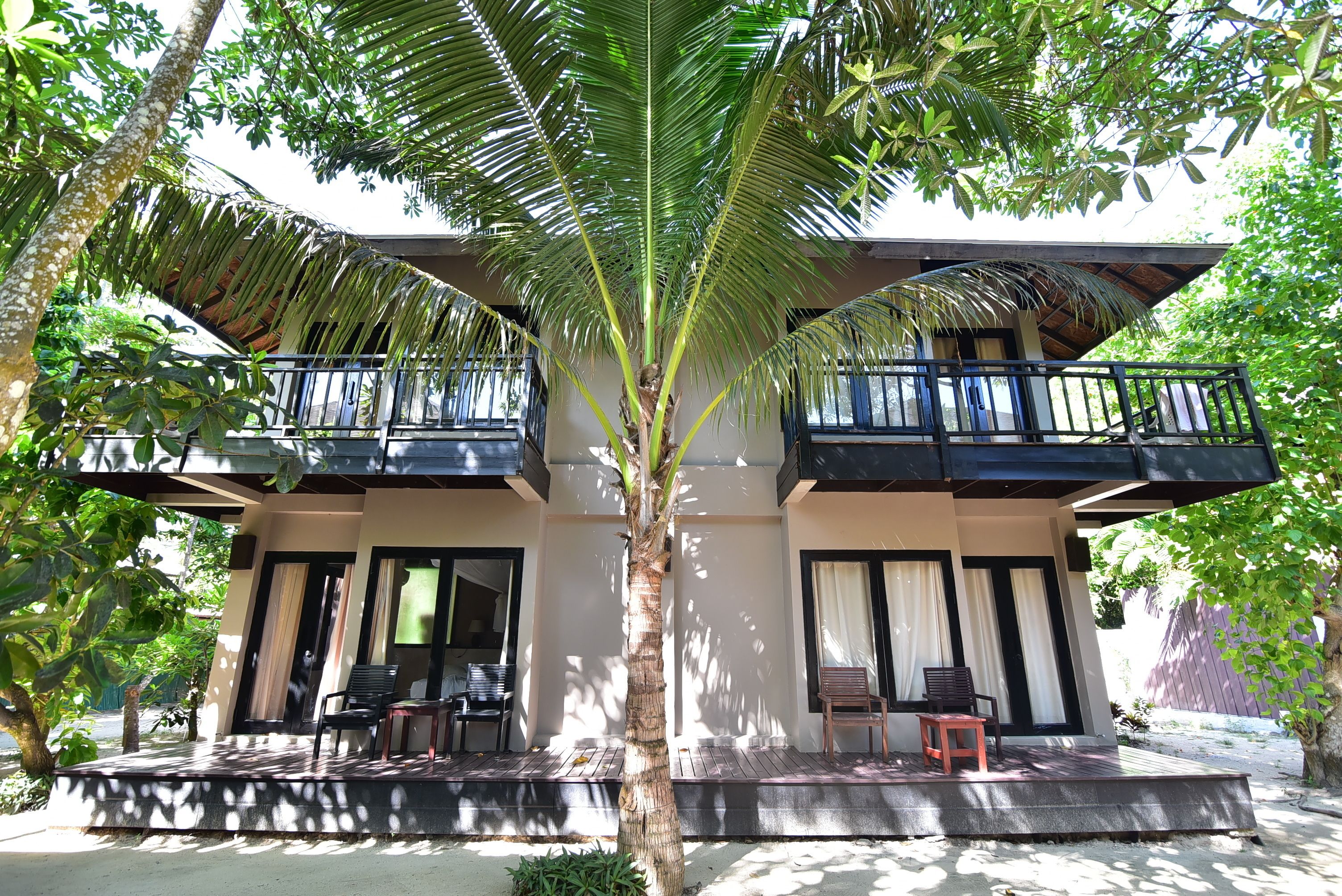 A two-story building with a balcony, outdoor seating, and a palm tree.