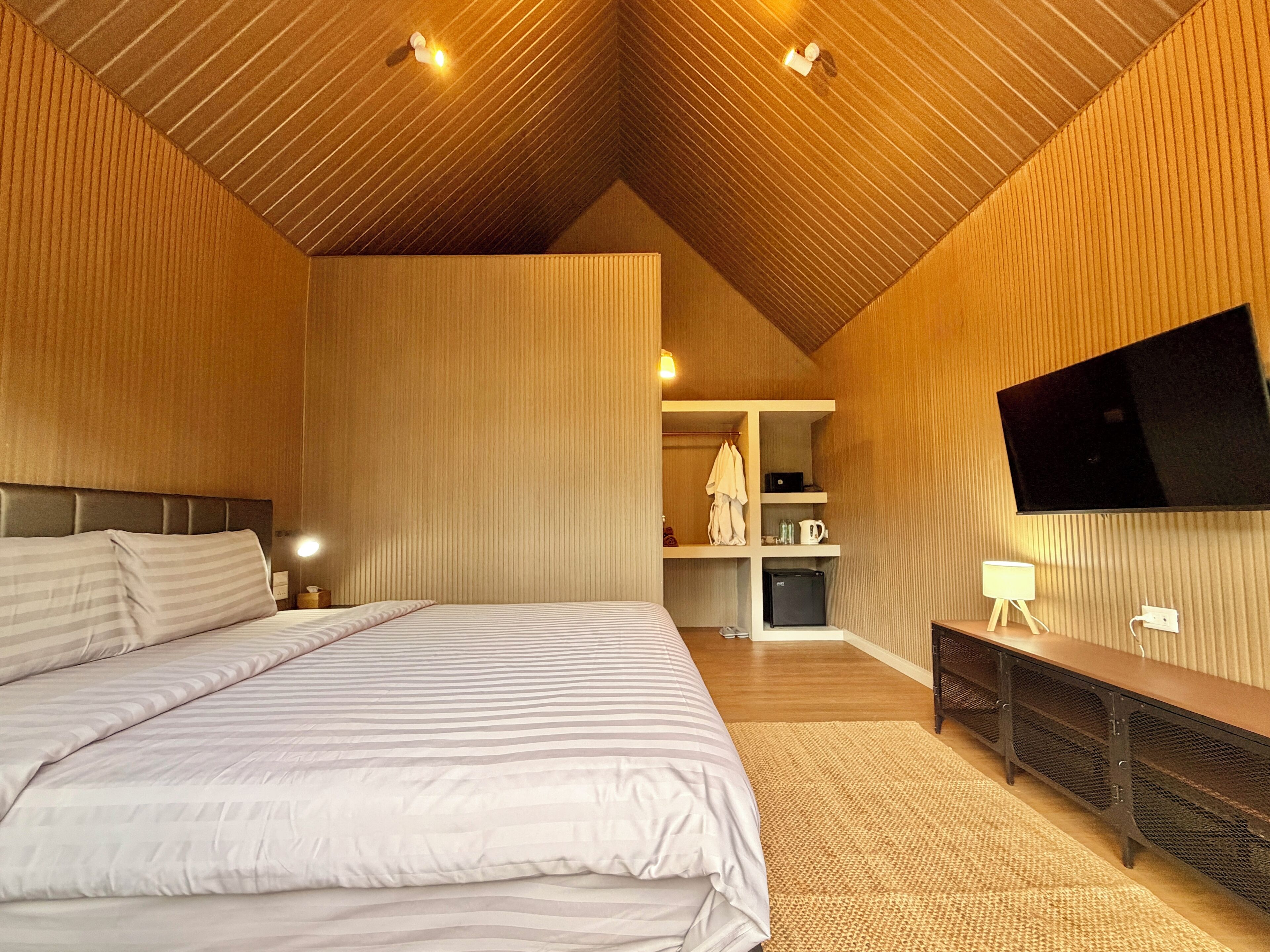 A bedroom with a large bed, a flat-screen TV mounted on the wall, and a built-in bench with storage.