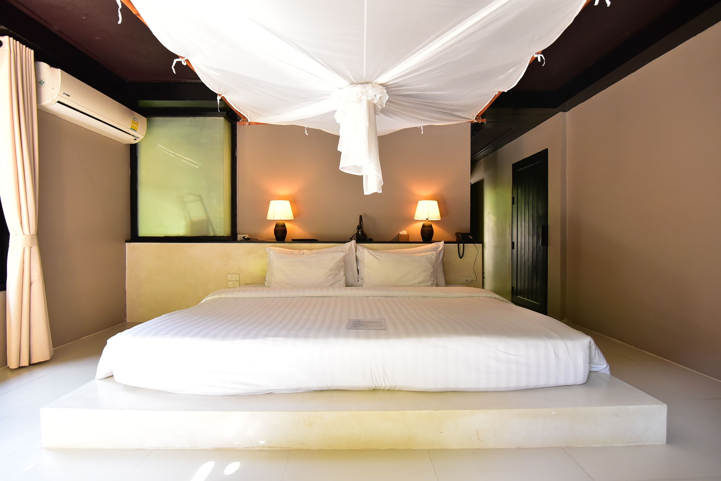 A large bed with white linens, two bedside lamps, and a ceiling draped with white fabric.