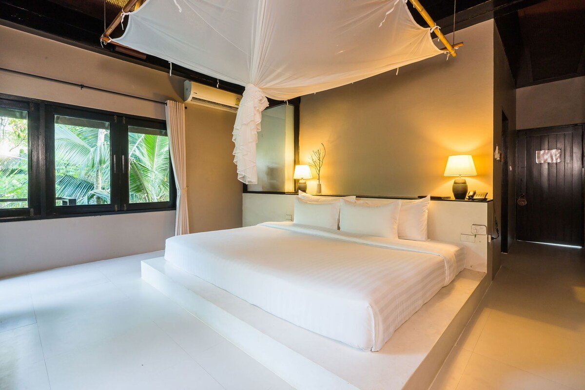 Una cama grande con ropa de cama blanca, dosel y dos lámparas de noche.