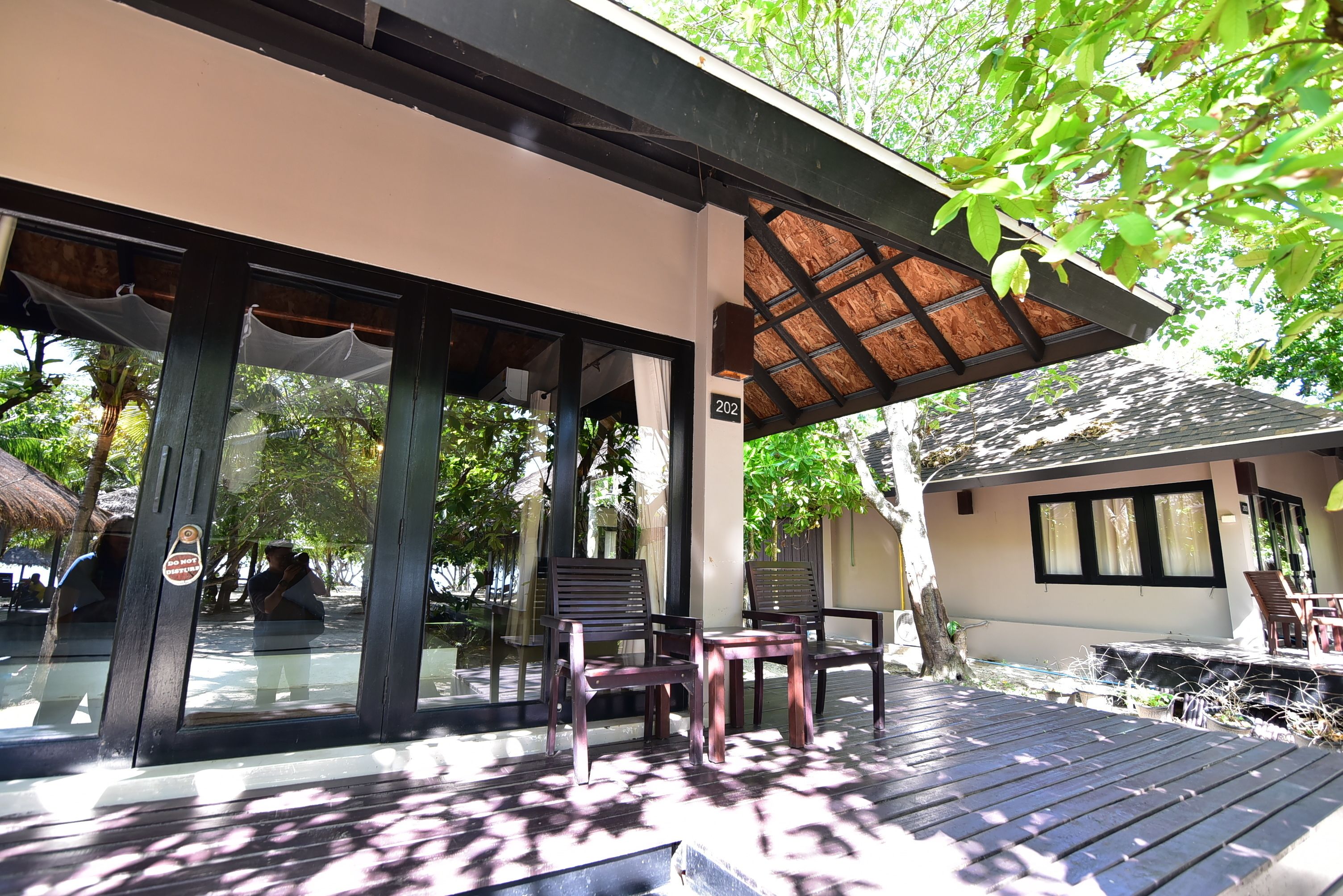 A covered outdoor seating area with wooden chairs and tables, a glass door entrance, and a building number 202 visible.