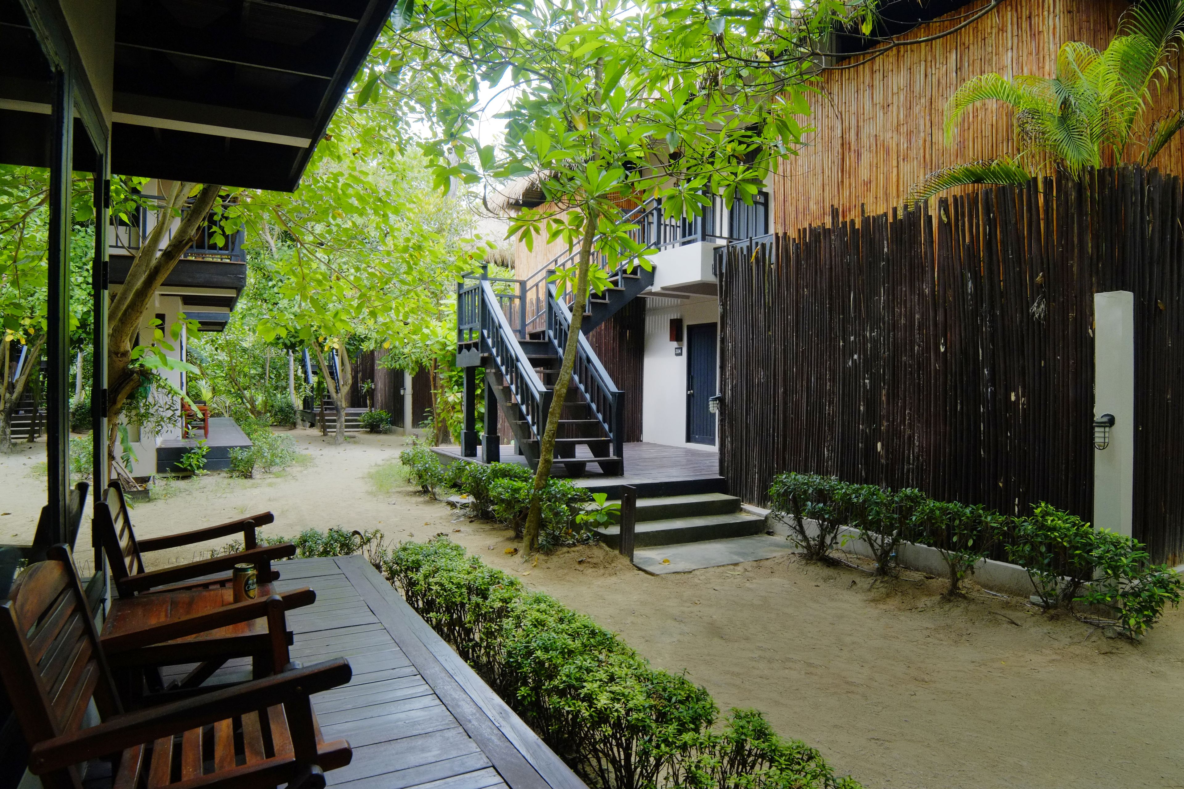 A courtyard with a wooden deck, a staircase, and a bamboo fence.