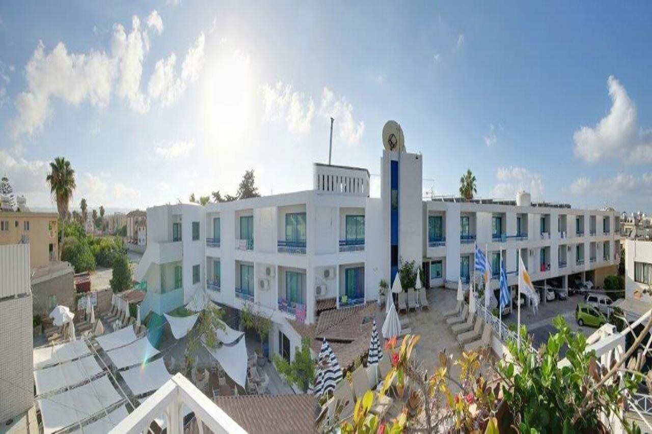 Ein mehrstöckiges Hotel mit einem zentralen Turm, Balkonen und einem Parkplatz.