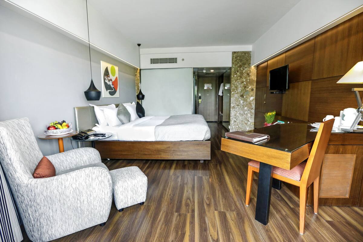 Una habitación de hotel moderna con una cama, un escritorio, una silla, un televisor y una mesita con un frutero.