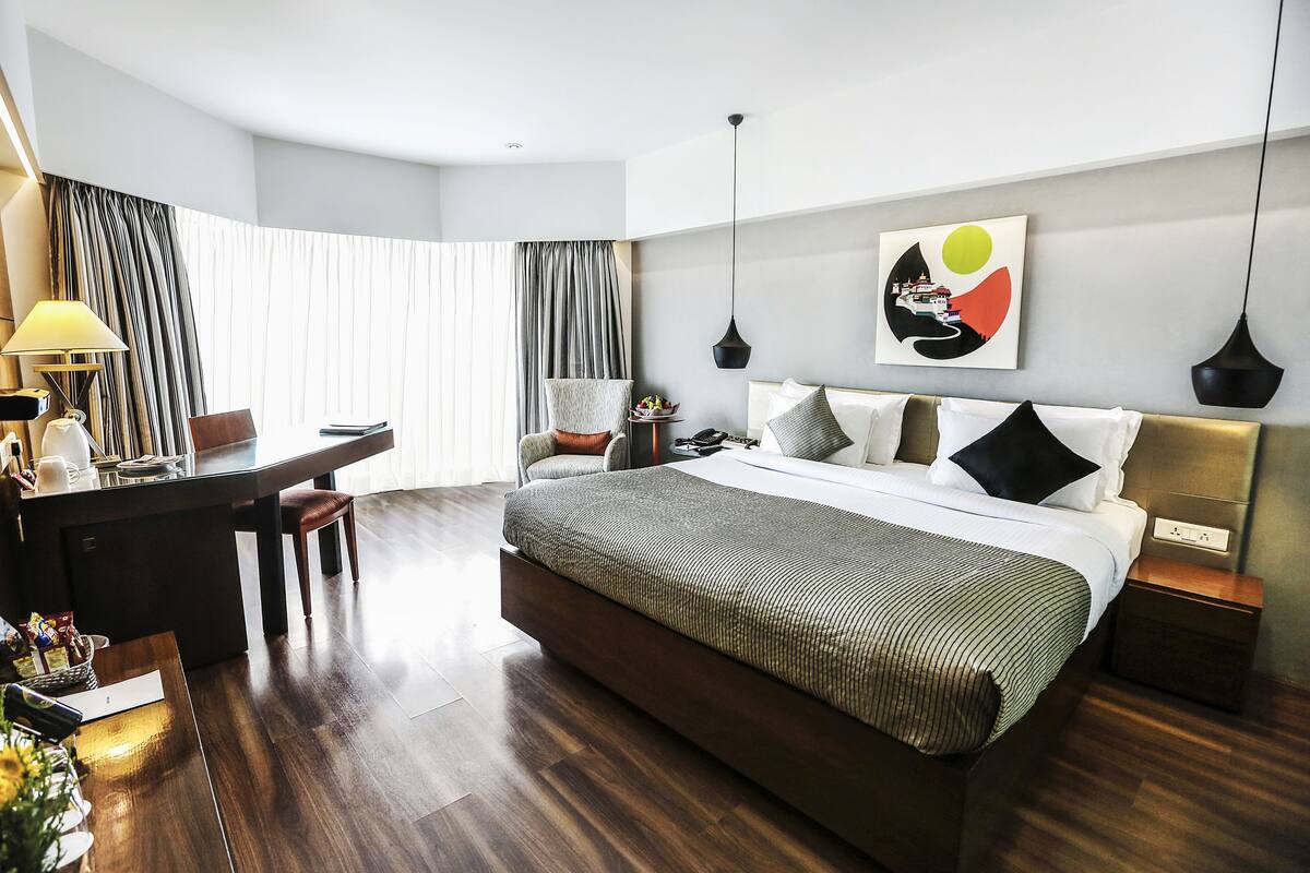 Habitación de hotel moderna con una cama grande, un escritorio y una silla. Hay un cuadro en la pared y una lámpara en el escritorio.