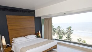 Ein modernes Hotelzimmer mit einem großen Bett, einem Nachttisch, einer Lampe und Blick auf den Strand.